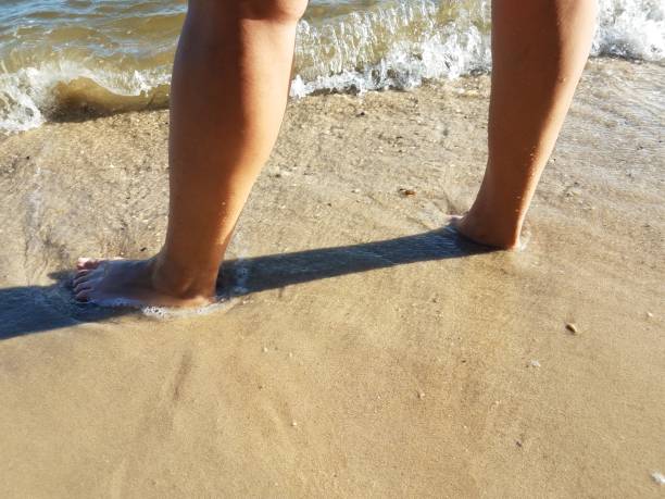 istock woman's feet standing in wet sand at beach 1323614337