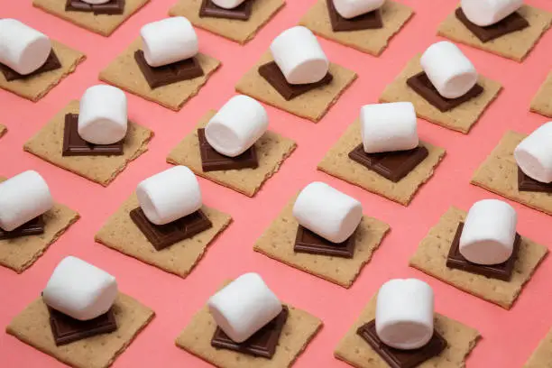 White marshmallow, chocolate bars and graham crackers on a pink background.
