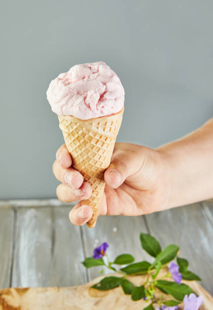 istock Hand holding waffle cone with ice cream on gray background with flowers 1323615201