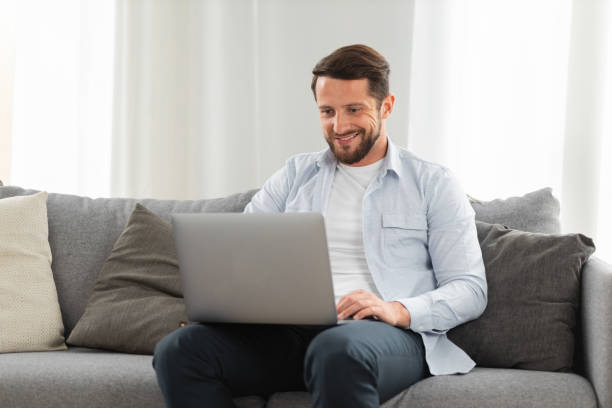 istock Happy caucasian man uses laptop computer for video call while sitting on sofa at home, smiling caucasian man chatting with friends or family via video conference on social networks 1323620537
