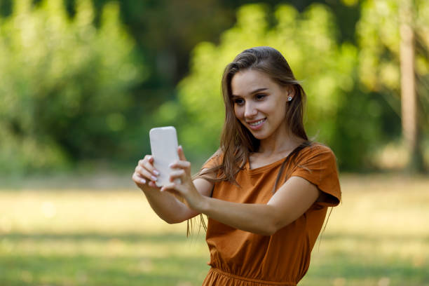 istock A Young Woman is Using a Mobile Phone to Make Self Portrait Photo While Walking in a Park. 1323624279