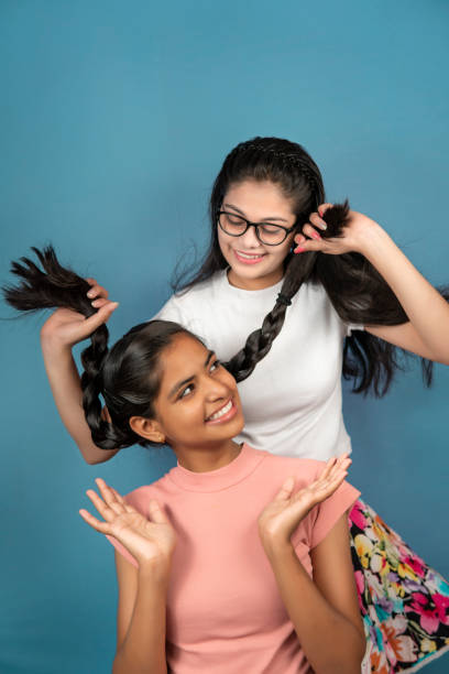 Portrait of happy two female best friends having fun over blue background. Image of pretty two happy female best friends having fun together against an isolated blue background. gay long hair stock pictures, royalty-free photos & images