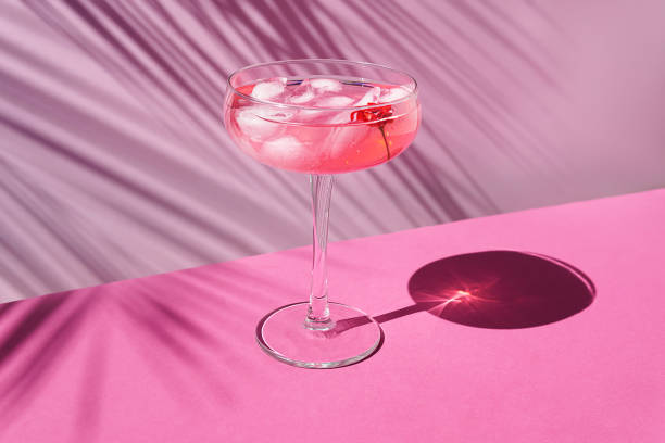 Pink champagne with ice on the table with sun shadows. Tropical concept. Pink champagne with ice on the table with sun shadows. On a pink background with palm leaves, front view. still life stock pictures, royalty-free photos & images