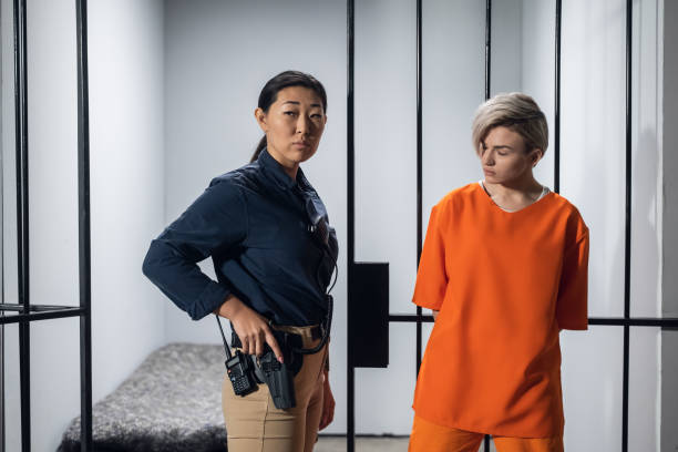 Blonde inmate in an asian women's general security prison is led out of her cell by a uniformed guard, with a holstered pistol and a walkie-talkie Blonde inmate in an asian women's general security prison is led out of her cell by a uniformed guard, with a holstered pistol and a walkie-talkie prison guard stock pictures, royalty-free photos & images