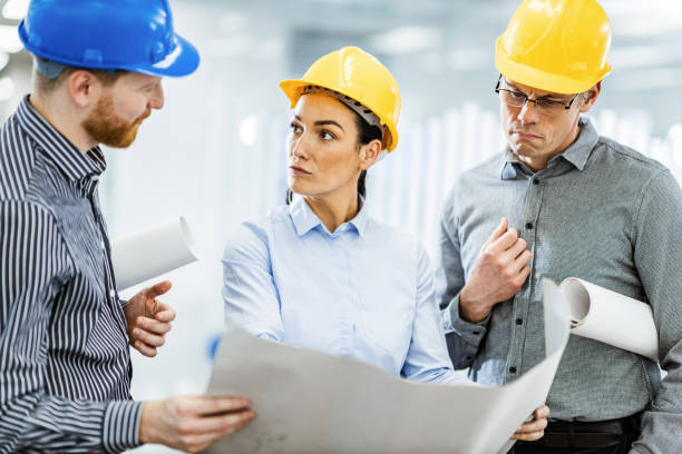 istock Group of architects talking while examining blueprints in the office. 1323635691
