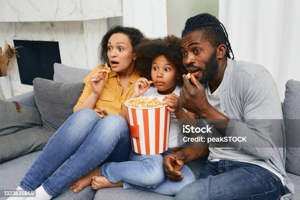 Father Mother And Child Sit On Sofa With Frightened Faces During Watching Scary Movie At Home Theater Stock Photo - Download Image Now