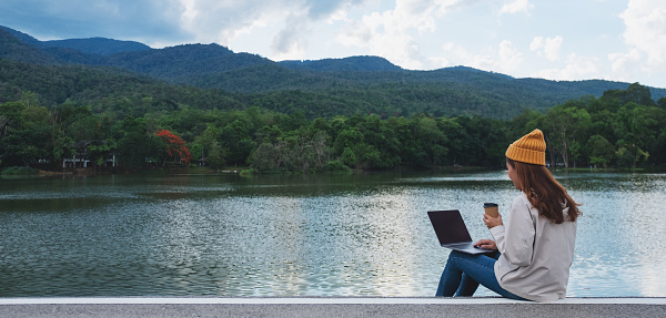A young woman using and working on laptop computer while traveling mountains and lake