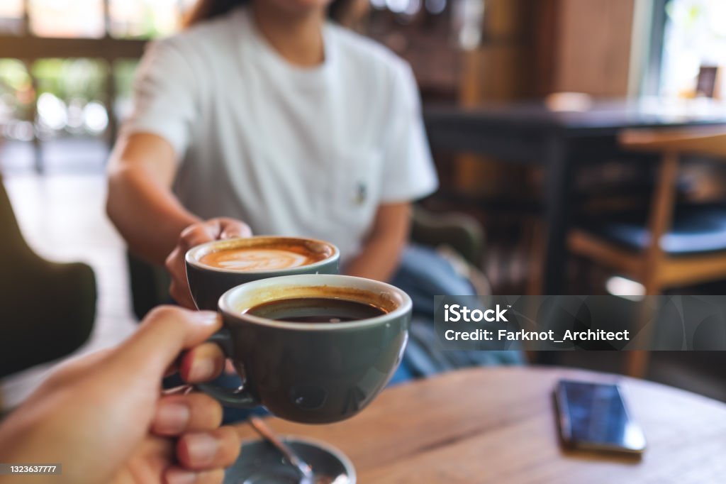 a man and a woman clinking coffee mugs in cafe Closeup image of a man and a woman clinking coffee mugs in cafe Coffee - Drink Stock Photo