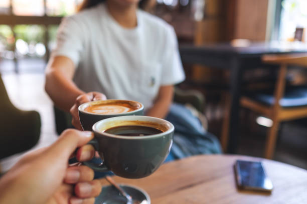 a man and a woman clinking coffee mugs in cafe stock photo