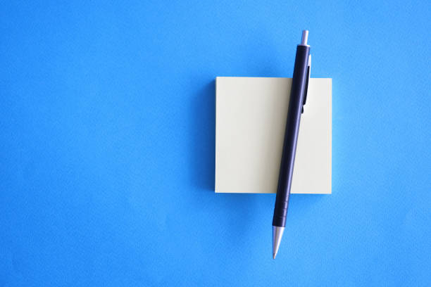 Ballpoint pen and paper stickers lying on blue background closeup Ballpoint pen and paper stickers lying on blue background closeup. Bad memory leave reminder concept leaving a tip stock pictures, royalty-free photos & images