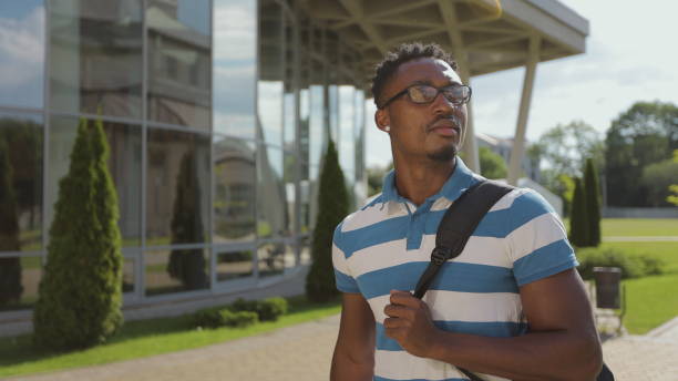istock Afro male student with backpack walking on university campus. Young afro american man with glasses walks the streets of a modern city with a backpack on his shoulders. 1323641134