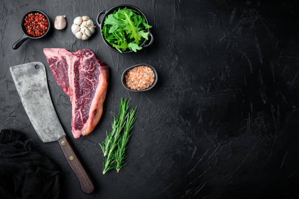 thick raw t-bone steak with seasoning and rosemary, on black stone background, top view flat lay, with copy space for text - veal t bone steak raw steak imagens e fotografias de stock