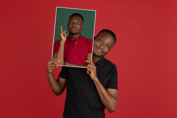istock Young african man holding his portrait isolated over red studio background with copyspace for ad. 1323644795
