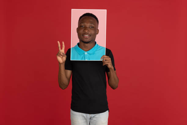 istock Young african man holding his portrait isolated over red studio background with copyspace for ad. 1323644797