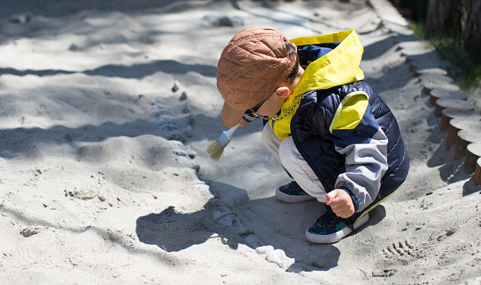 Boy playing paleontologist , cleaning bone from the sand with brush