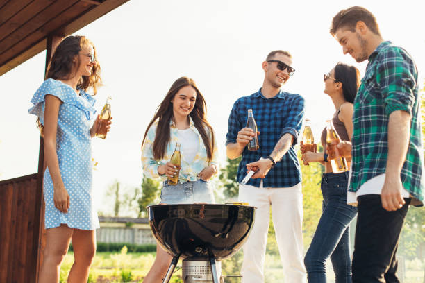 istock Group of people standing around a barbecue, grilling outdoors, chatting and drinking drinks, outdoors in the summer in 1323647351
