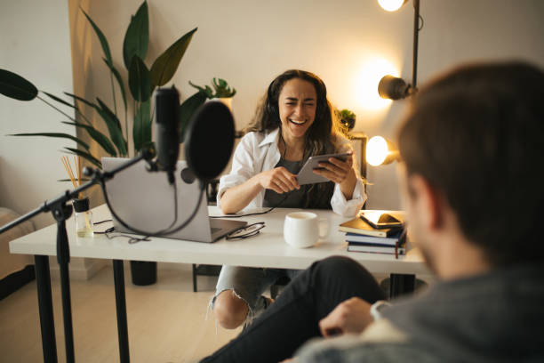 istock Young woman blogger interviewing hipster man in a studio, using microphone and laptop. 1323648778