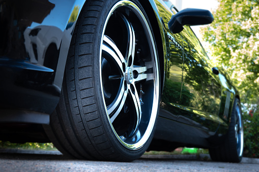 Hamburg, Germany - June 13. 2021: Close-up from a low perspective with focus on the right front tire of a black Chevrolet Camaro, parked somewhere in Hamburg, Germany
