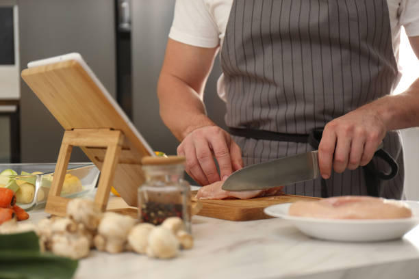 istock Man cutting chicken fillet while watching online cooking course via tablet in kitchen, closeup 1323651612