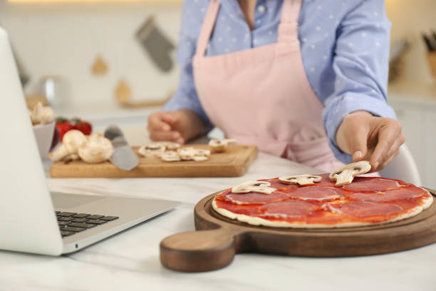 istock Woman making pizza while watching online cooking course via laptop in kitchen, closeup 1323652661