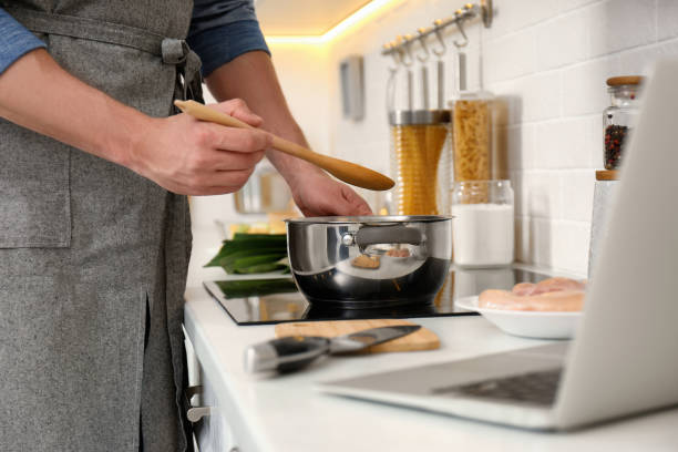 Man making dinner while watching online cooking course via laptop in kitchen, closeup
