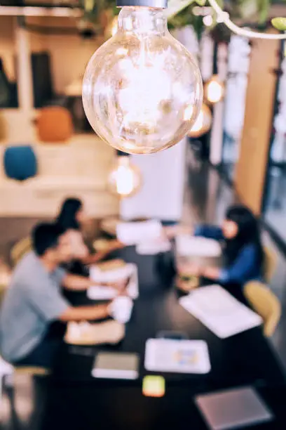 Photo of Shot of a lightbulb hanging over a group of creatives working together