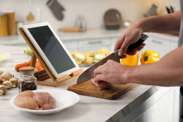 istock Man cutting chicken fillet while watching online cooking course via tablet in kitchen, closeup 1323652775