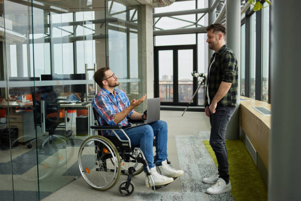 istock Disabled computer programmer discussing with male coworker in office hallway 1323653812