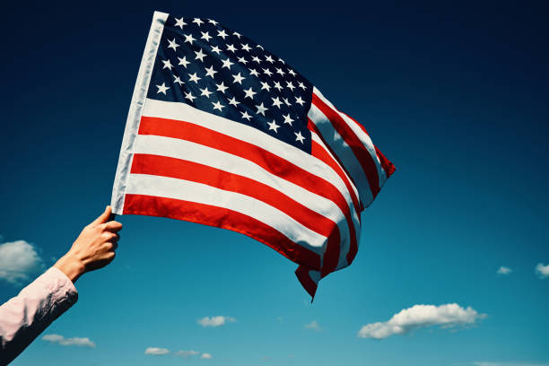 istock Waving usa flag in hand against blue sky 1323653910