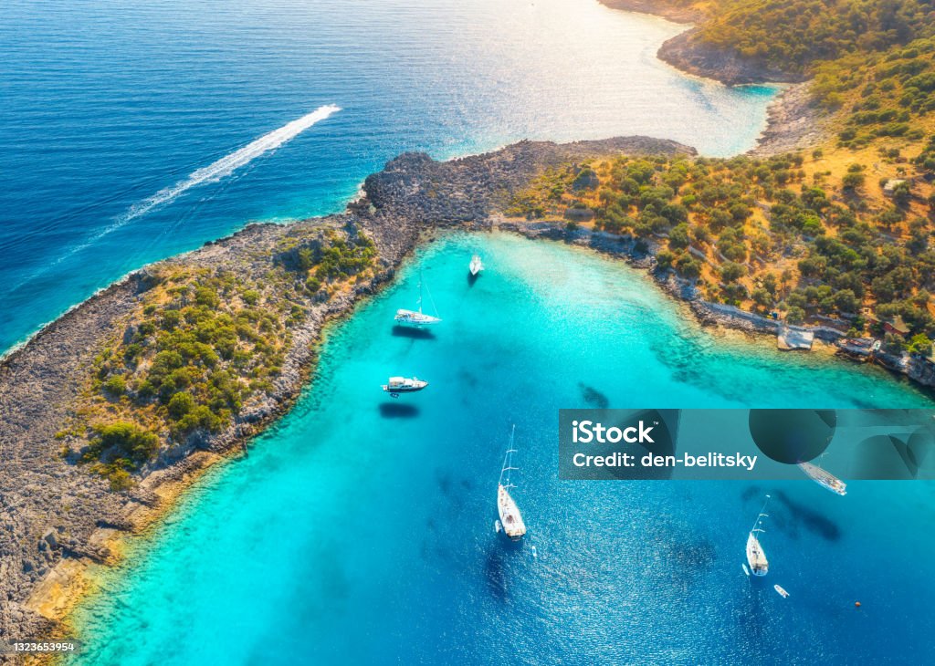 Aerial view of beautiful yachts and boats on the sea at sunset in summer. Akvaryum koyu in Turkey. Top view of luxury yachts, sailboats, clear blue water, rock, sky, mountain and green trees. Travel Türkiye - Country Stock Photo