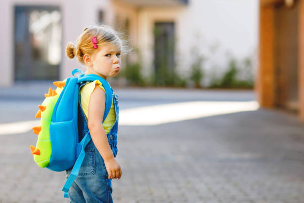 Cute little adorable toddler girl on her first day going to playschool. Healthy upset sad baby walking to nursery school. Fear of kindergarten. Unhappy child with backpack on the city street, outdoors Cute little adorable toddler girl on her first day going to playschool. Healthy upset sad baby walking to nursery school. Fear of kindergarten. Unhappy child with backpack on city street, outdoors way to school stock pictures, royalty-free photos & images