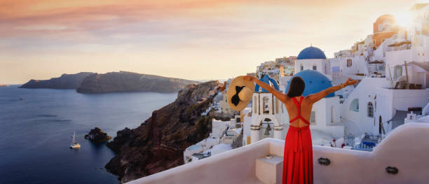 kobieta turystyczna w czerwonej sukience cieszy się panoramicznym widokiem na wioskę oia podczas zachodu słońca - hat oia europe vacations zdjęcia i obrazy z banku zdjęć