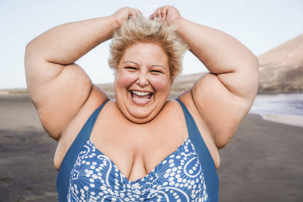 istock Curvy woman smiling on camera wearing bikini with beach in background - Focus on face 1323655422