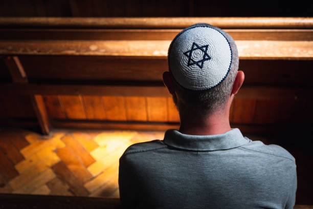 istock Young Jewish man wearing skull cap praying inside synagogue 1323656068