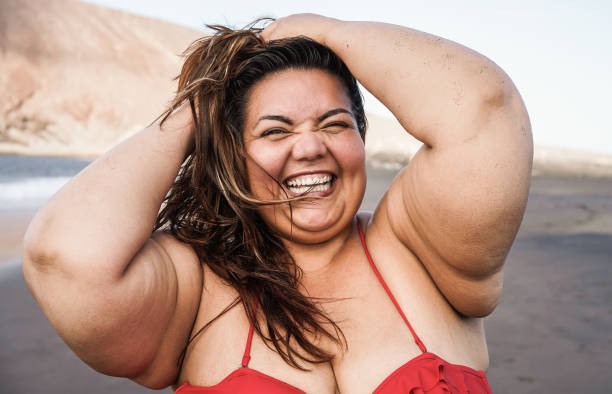 istock Plus size woman smiling on camera wearing bikini with beach in background - Focus on face 1323656878