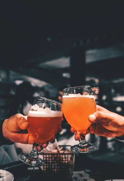 nahaufnahme eines zwei glases bier in der hand. biergläser klirren in bar oder pub - lagerbier stock-fotos und bilder