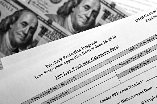 selective focus monochrome photo of paycheck protection program loan forgiveness application form revised, on a background of dollar bills