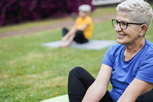 senior people doing yoga class keeping social distance at city park - focus on right woman face - women yoga yoga class mature adult imagens e fotografias de stock