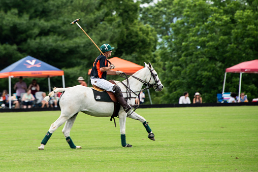 Crozet, Virginia, USA - June 13, 2021: An exciting polo match played on June 13, 2021. The two teams playing are Acme and Thalhimer. The teams consist of mixed male and female players. Spectators can be seen lining the field enjoying the game with chairs and tents and enjoying wine and food. A polo player is riding his horse to join his team mates at the other end of the field.