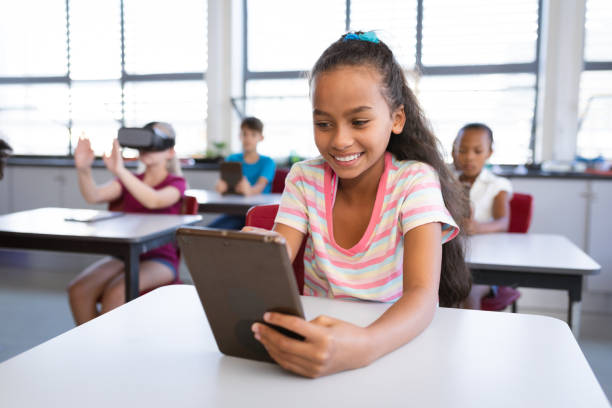 istock Smiling african american girl using digital tablet while sitting on her desk in class at school 1323664306