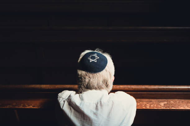 istock Senior Jewish man wearing skull cap praying inside synagogue 1323665538
