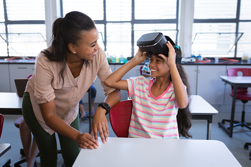 African american female teacher teaching a girl to use vr headset in the class at school. school and education concept