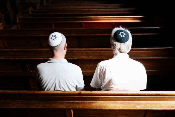 Jewish men sitting together and praying inside synagogue Close up image depicting a rear view of two Jewish men sitting together inside a synagogue. They have their heads bowed in prayer and they are wearing the traditional Jewish skull cap - otherwise known as a kippah or yarmulke - on their heads. Horizontal color image with copy space. rabbi photos stock pictures, royalty-free photos & images