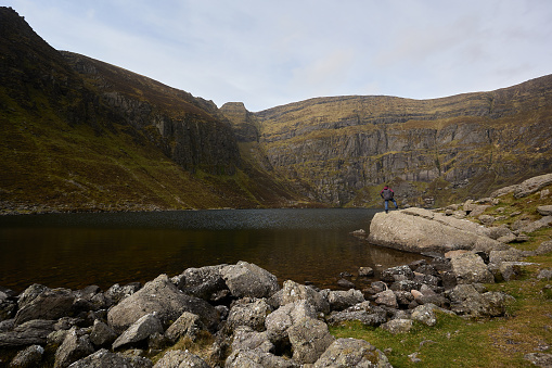 mountaineer man looking at a lake formed in a valley of mountains. Comeragh Mountains, Waterford, Ireland