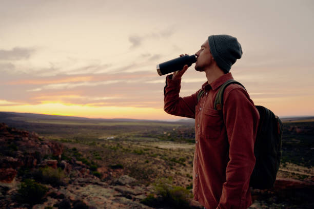 istock Thirsty male traveller drinking water on reaching cliff edge during morning 1323672891