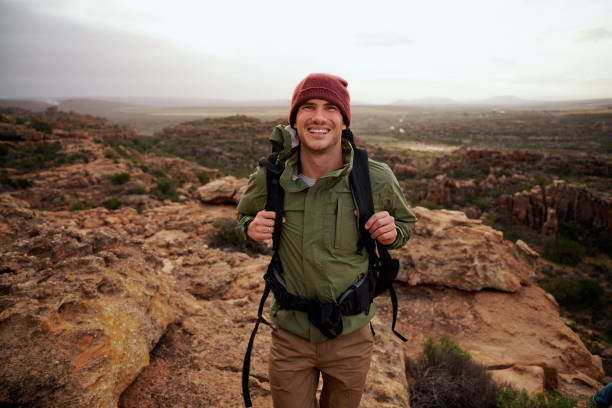 istock Portrait of happy active young man with backpack climbing mountain trail 1323674476