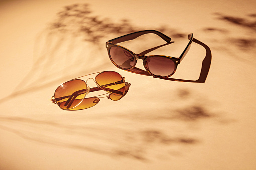 2 pairs of women sunglasses on a soft orange background and strong shadows of flowers