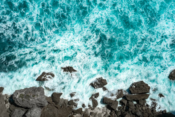 istock Raging blue ocean waves break on rocks with foam on the water 1323675949
