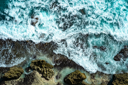 Raging blue waves of the ocean run and break on the rocks, top view