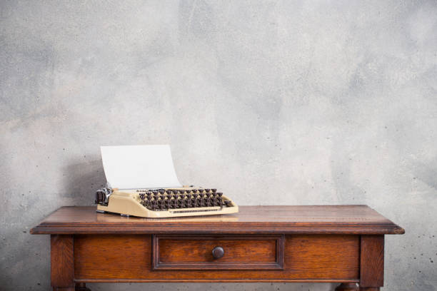 istock Old typewriter with paper blank on retro wooden table front concrete wall background. Vintage style filtered photo 1323677250